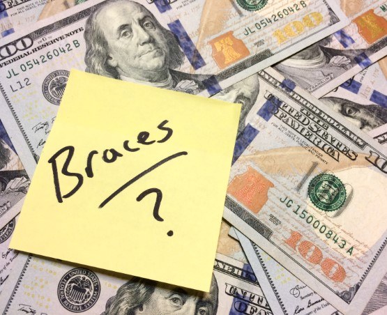 A sticky note labelled ‘braces’ sitting on top of hundred-dollar bills